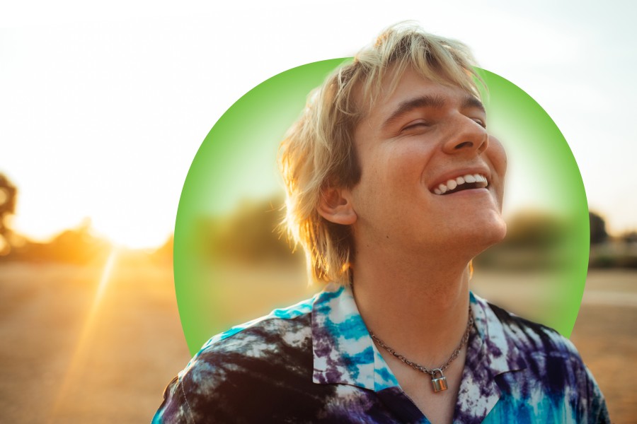 A young person standing outside in a field. They are smiling with their eyes closed. 