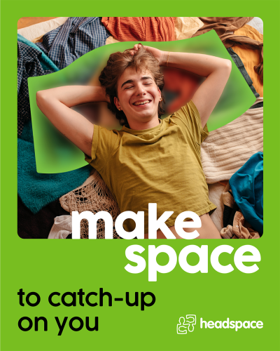 A young person laying on their bed on a pile of clothes. The young person is smiling and laying on their back with their hands behind their head.