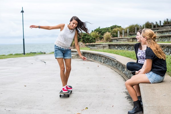 A female riding a skateboard with two friends watching.
