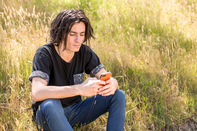 Young person texting on phone in a field.