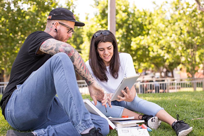 Two people studying together in a park, using tablets and books