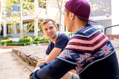 Person in vibrant sweater and red cap chats to a friend