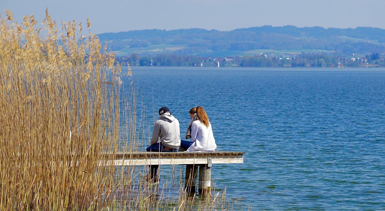 2 people sitting by water on pier