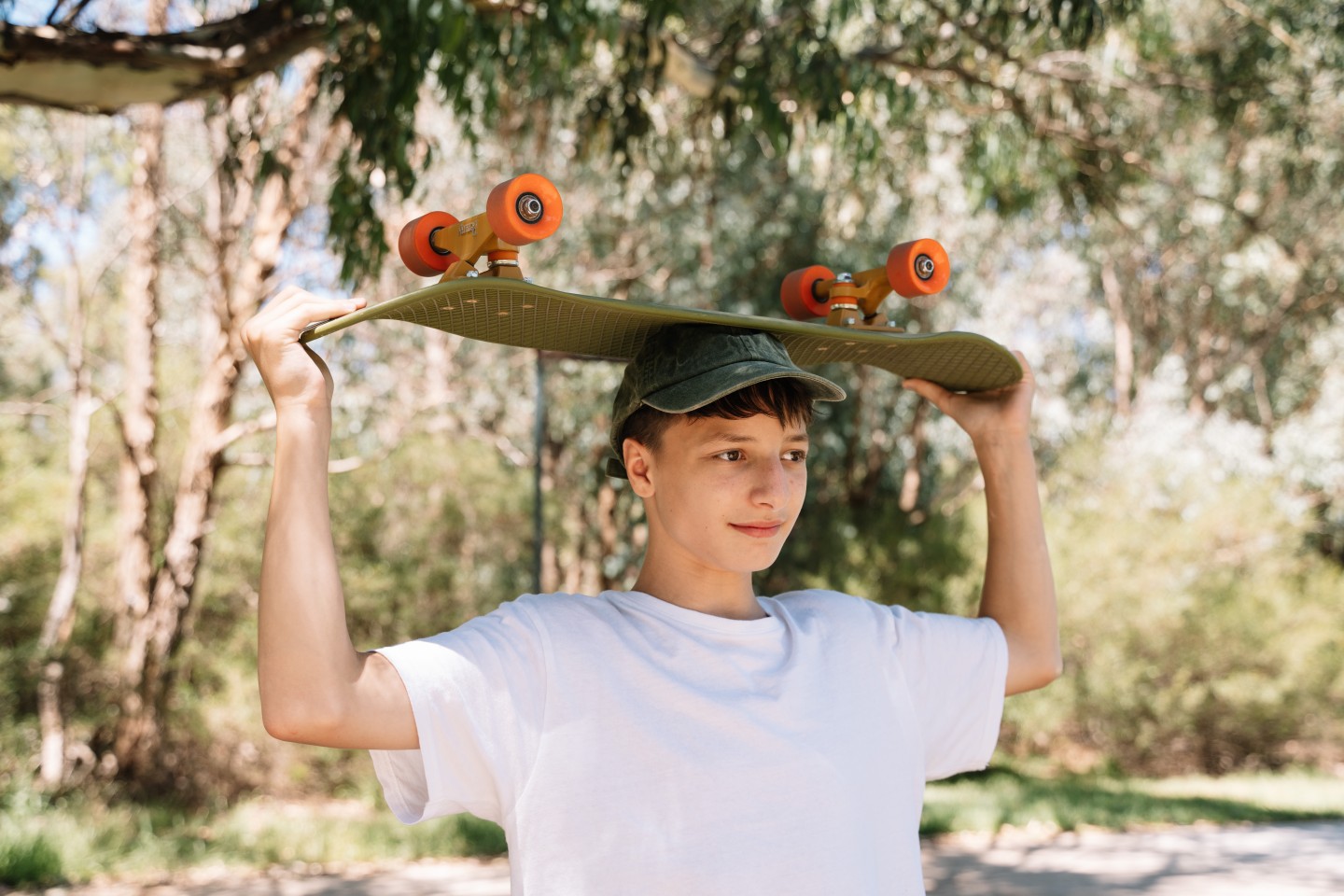 Teenage boy, holding a skateboard above his head.