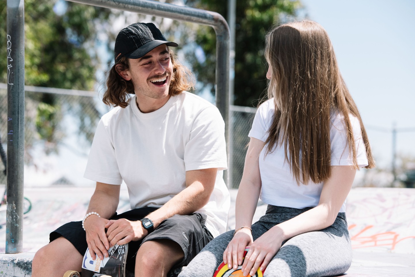 Two young people, sitting at a skate park, talking to each other.