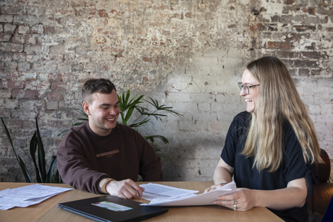 A young person and a headspace Work Study Specialist sitting a table smiling and looking at documents