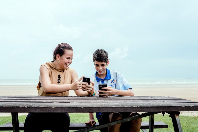 Two young people on their phones by the beach