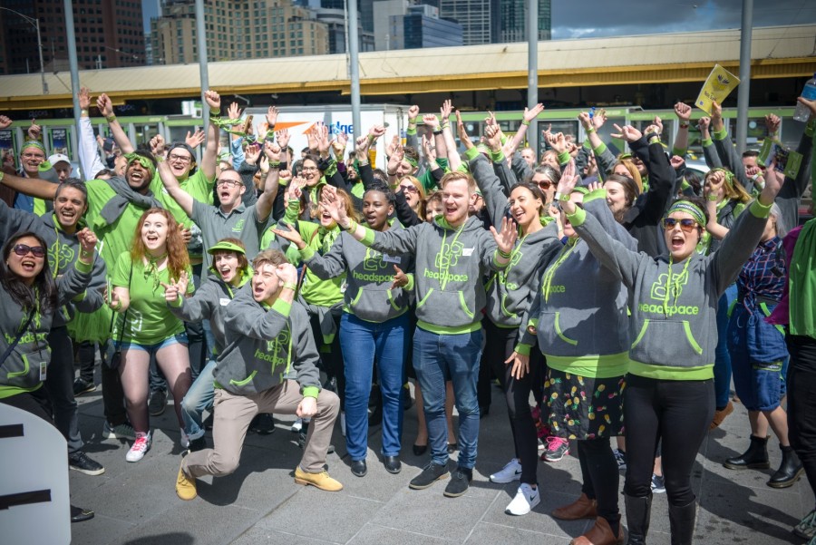 Large group of people in headspace branded clothing waving their arms up outside on headspace day