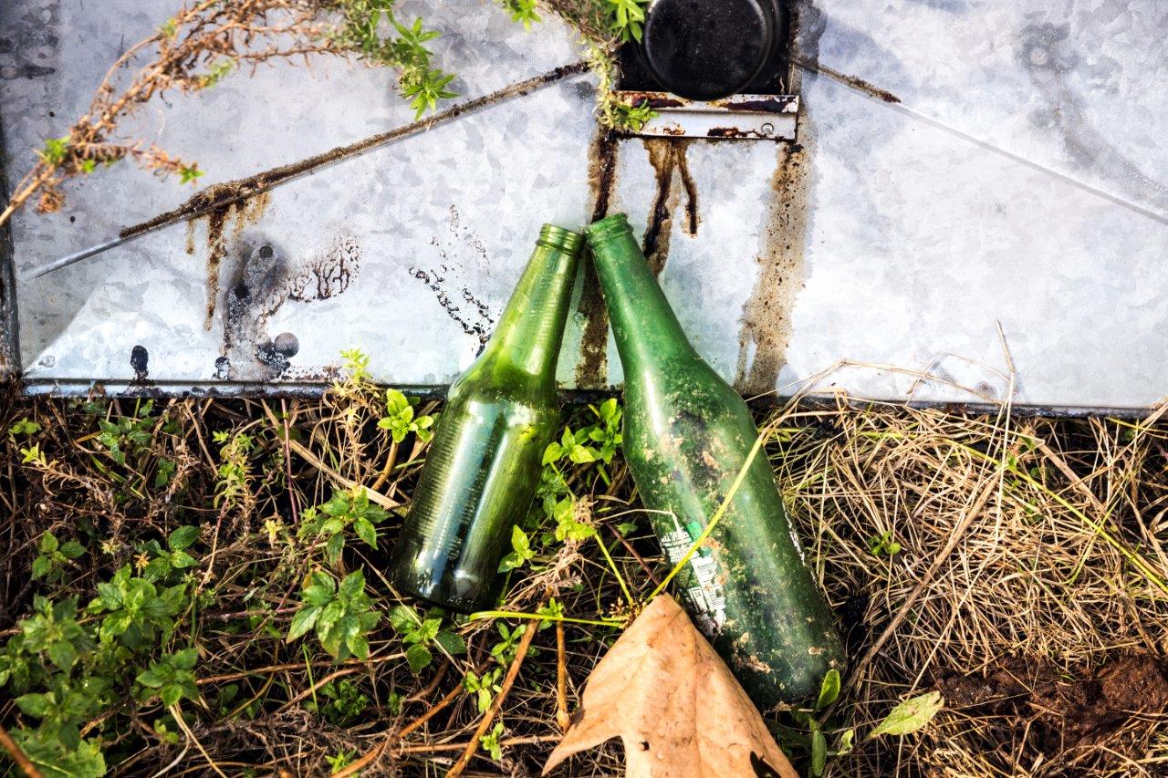 Two empty green bottles left on grass and garden tile