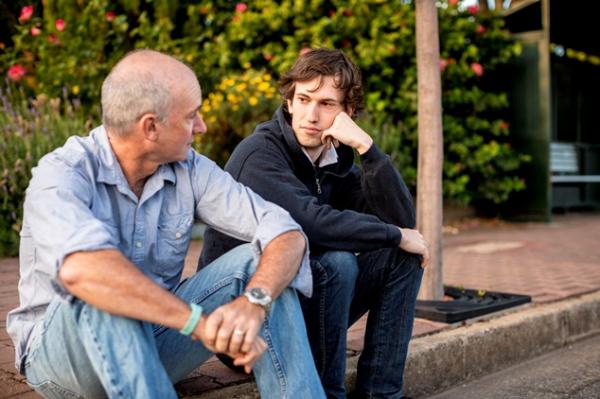 Young person sat with father on sidewalk curb.