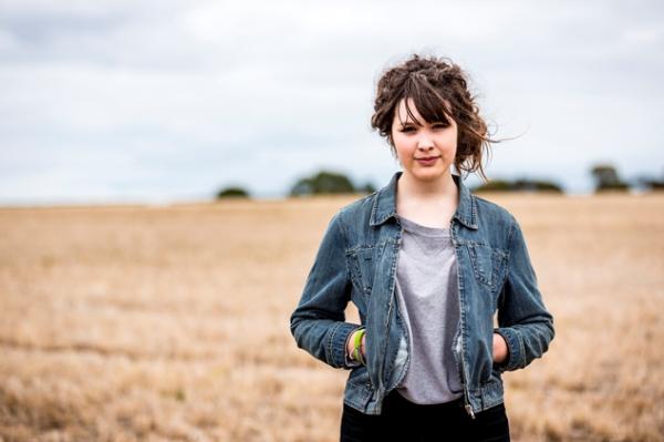 Young person in denim jacket stands in a wheat field.