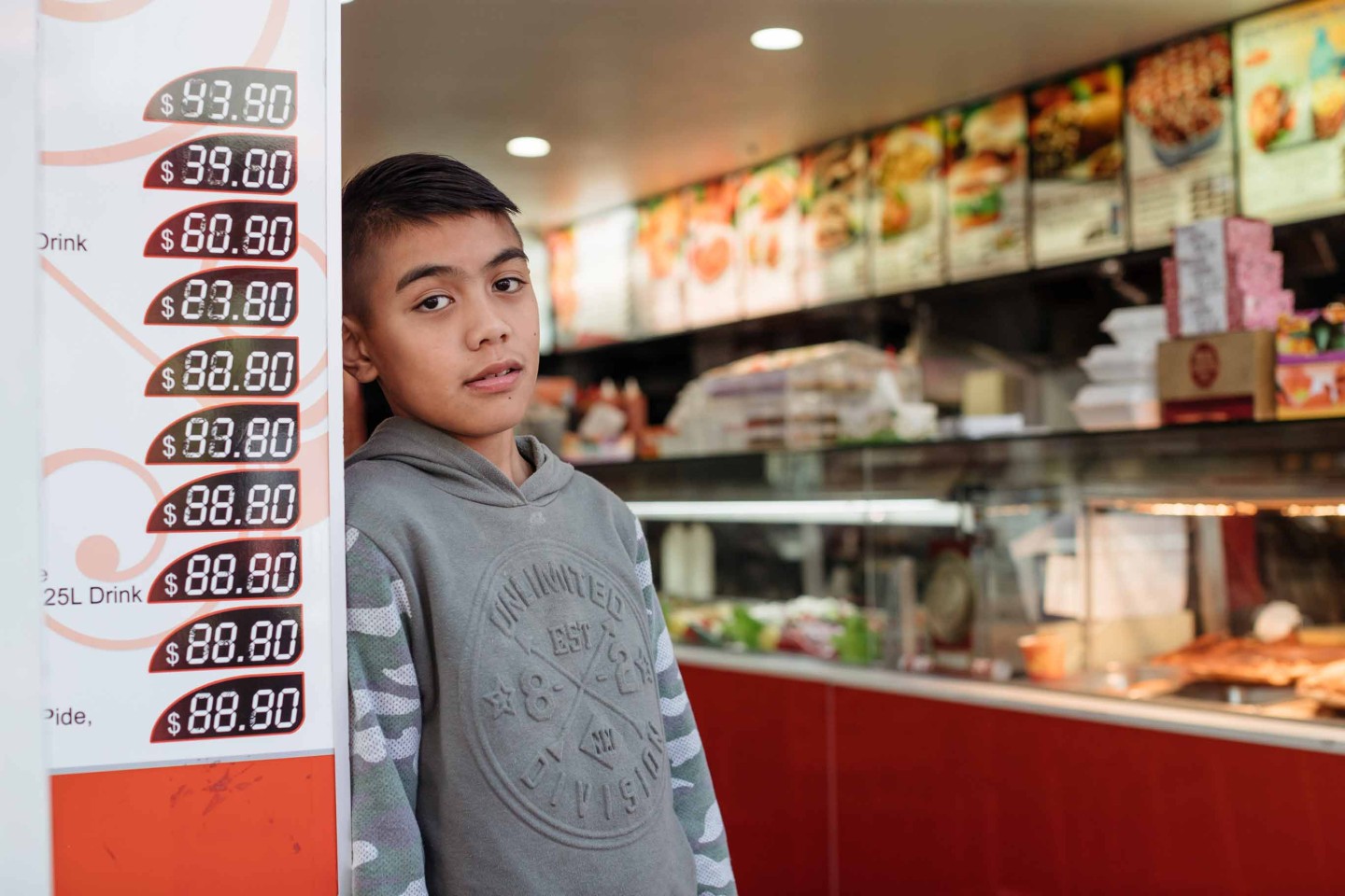 A young person leans against the wall of a takeaway shop