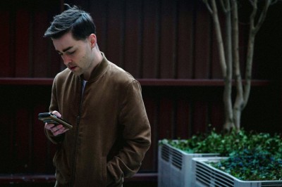 male in brown jacket looking down at his phone