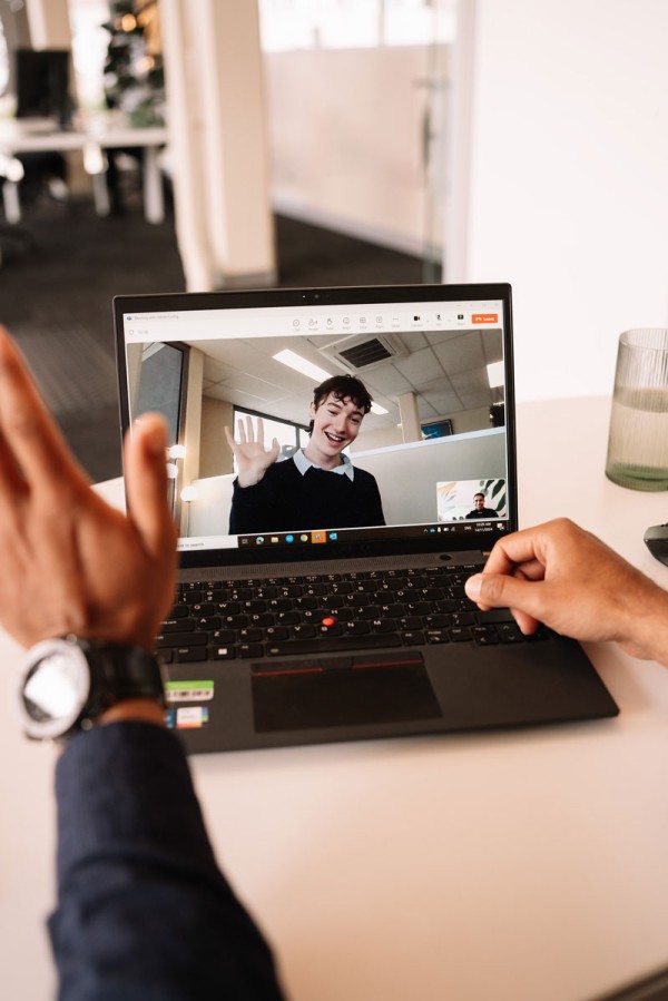 Laptop video call shown with young person waving on the screen